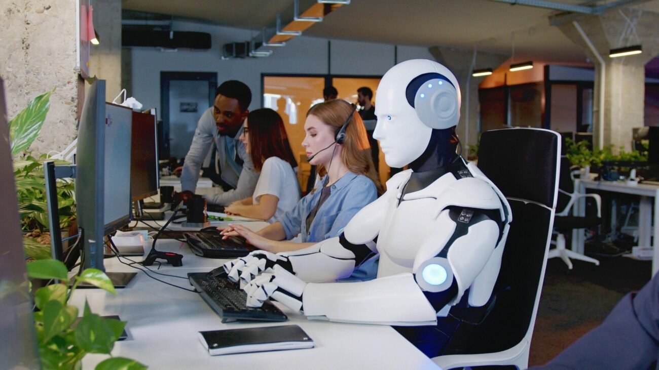 A humanoid robot typing at a keyboard in an office.