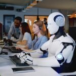 A humanoid robot typing at a keyboard in an office.